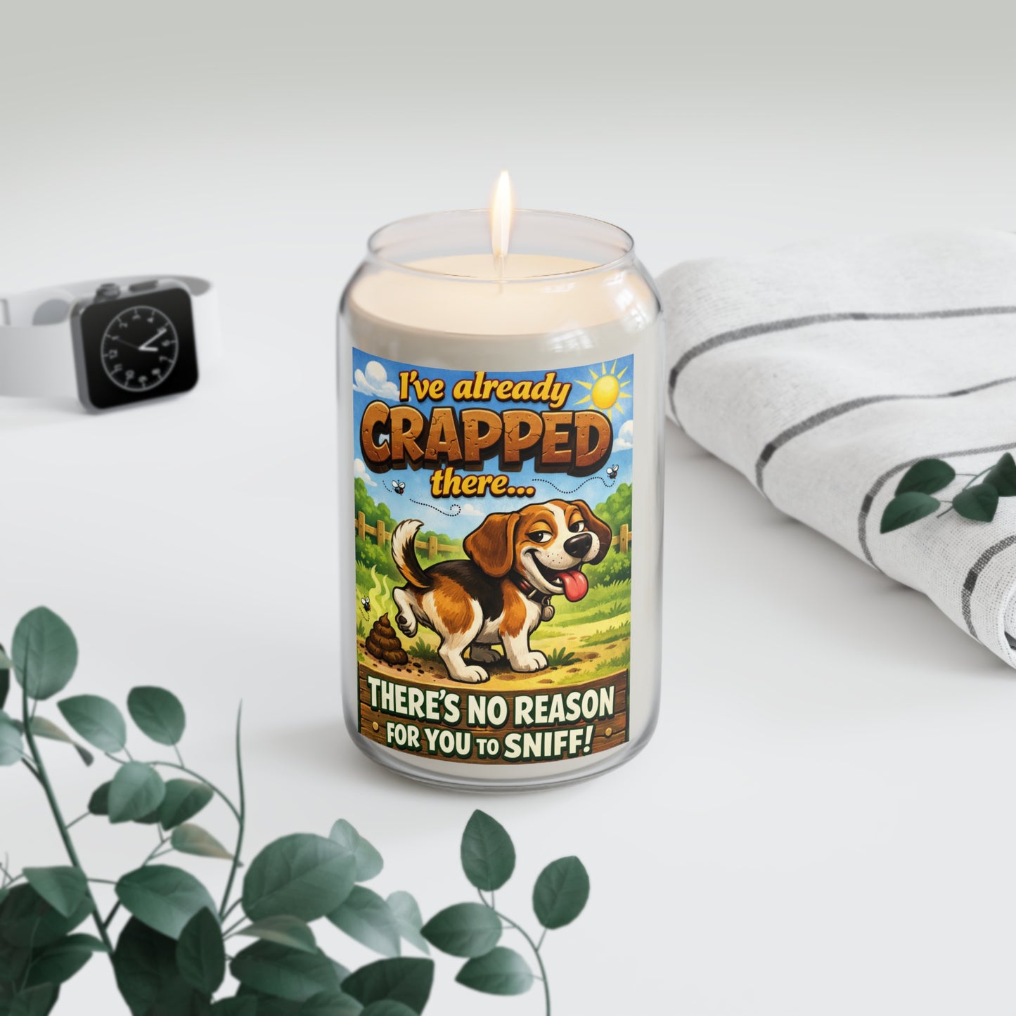 Candle with a dog-themed label on a white surface with a plant and watch in the background